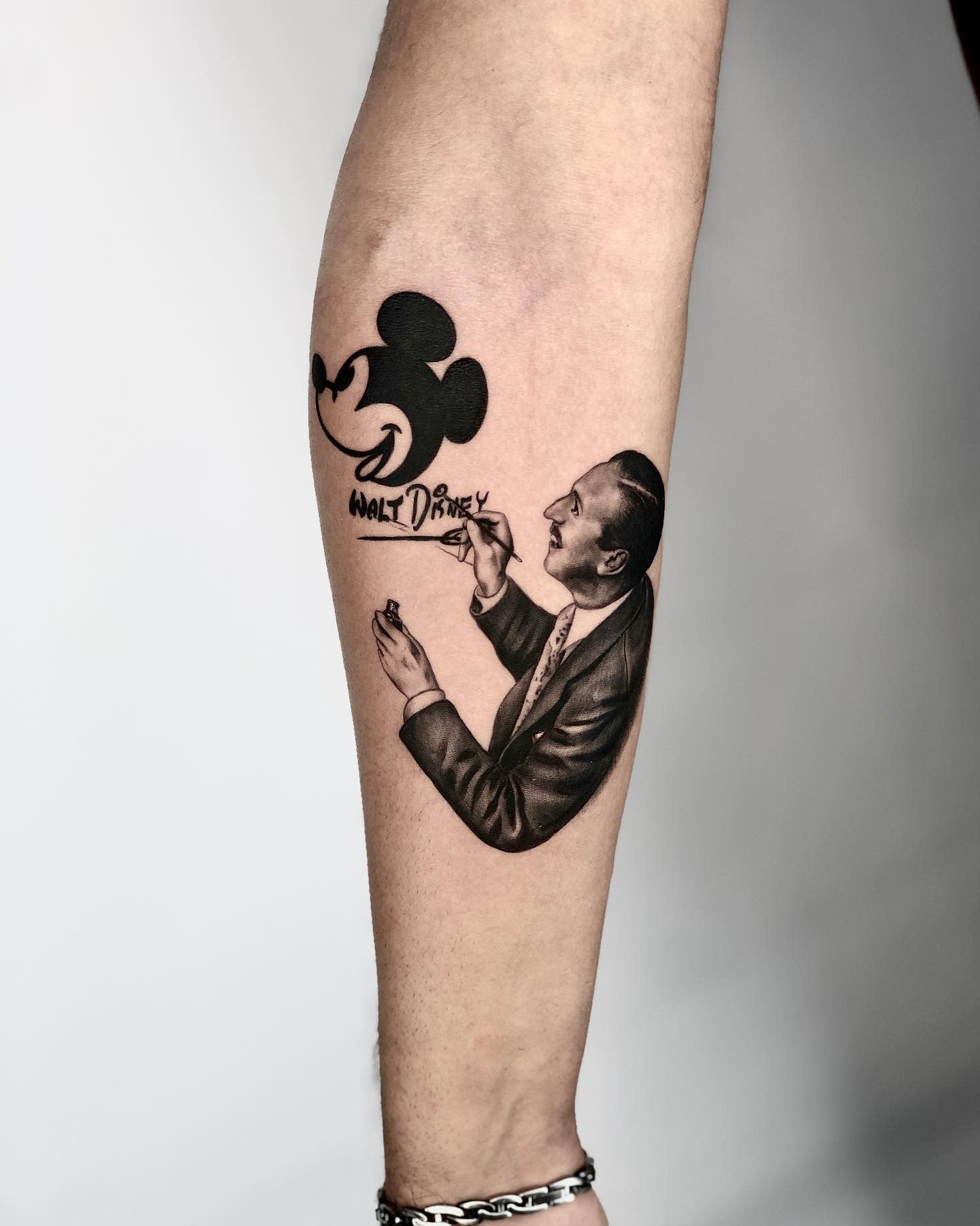 Black-and-gray tattoo of Walt Disney drawing Mickey Mouse, with his signature below the illustration